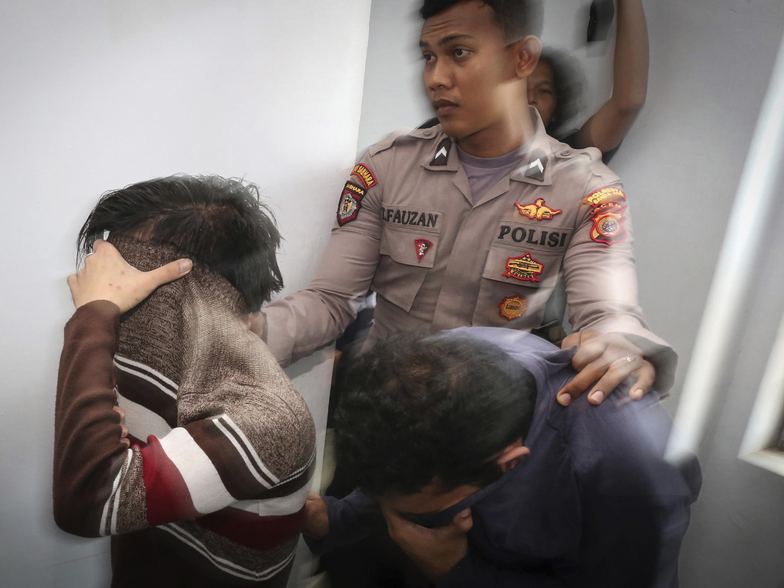 A police officer escorts two men accused of having gay sex into a holding cell prior to their trial at sharia court in Banda Aceh