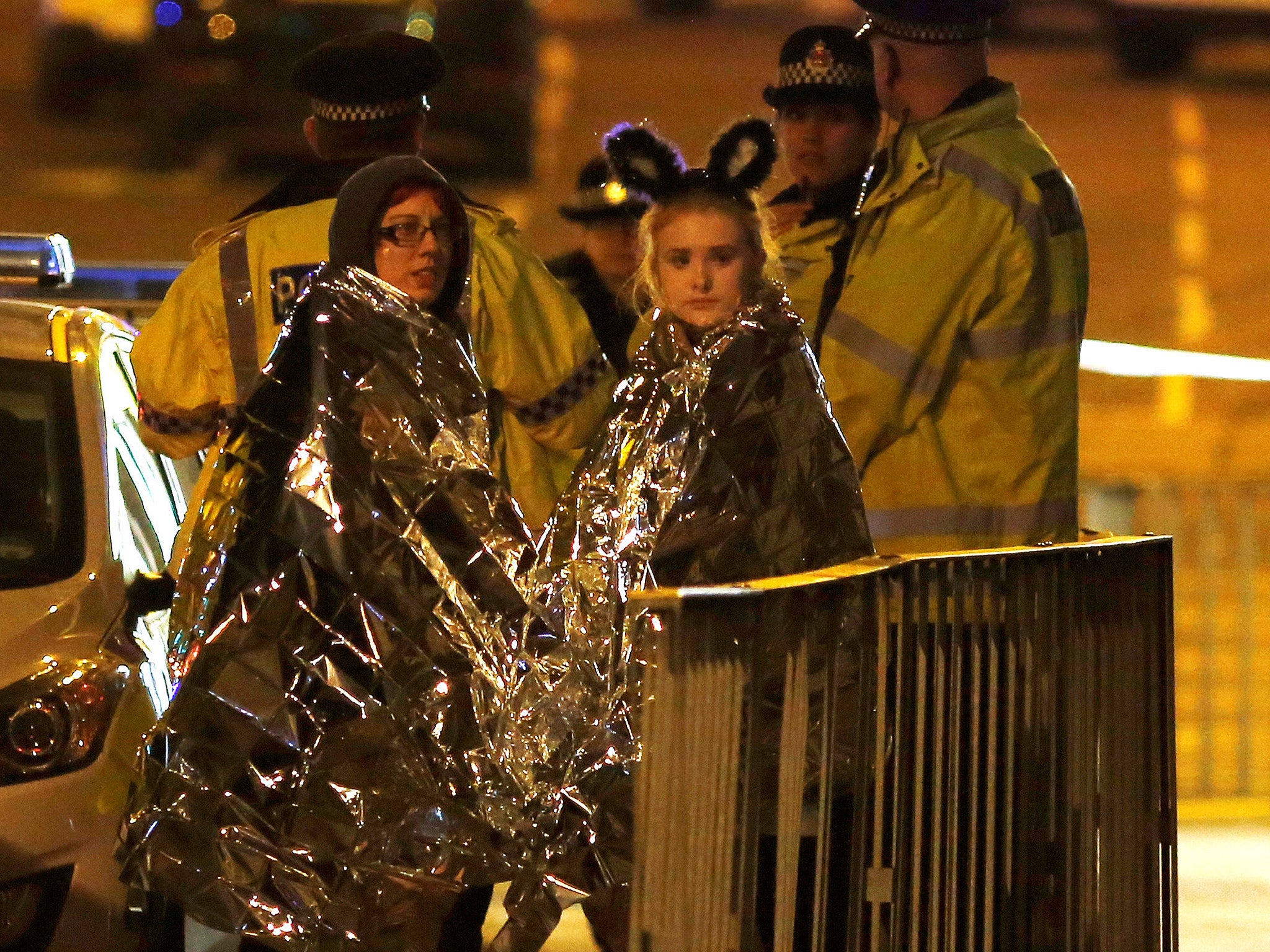 Two women wrapped in thermal blankets stand near the Manchester Arena, where Ariana Grande had been performing