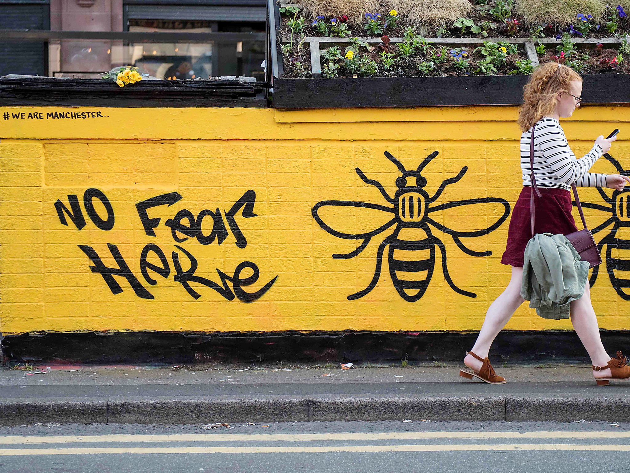 A woman passes a street-art graffiti mural, created following the May 22 terror attack at the Manchester Arena, featuring bees, which are synonymous with Manchester as a symbol of the city's industrial heritage, in Stevenson Square, Manchester
