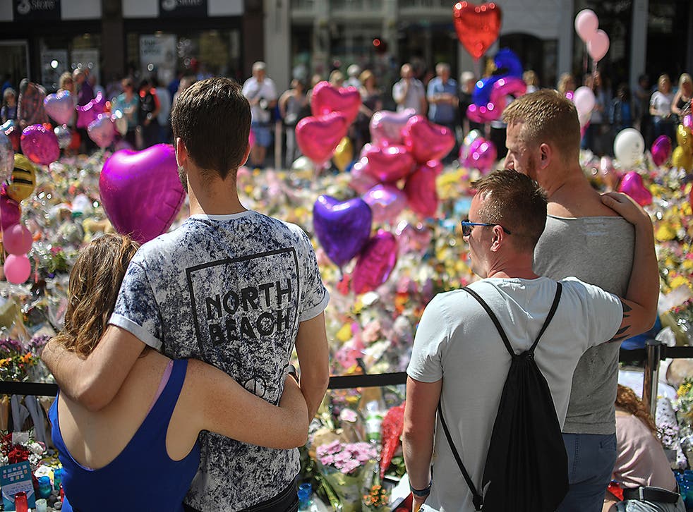 Couples comfort one another as flowers and balloons are left in Saint Ann's Square in tribute to those killed in an explosion at the Manchester Arena earlier this week