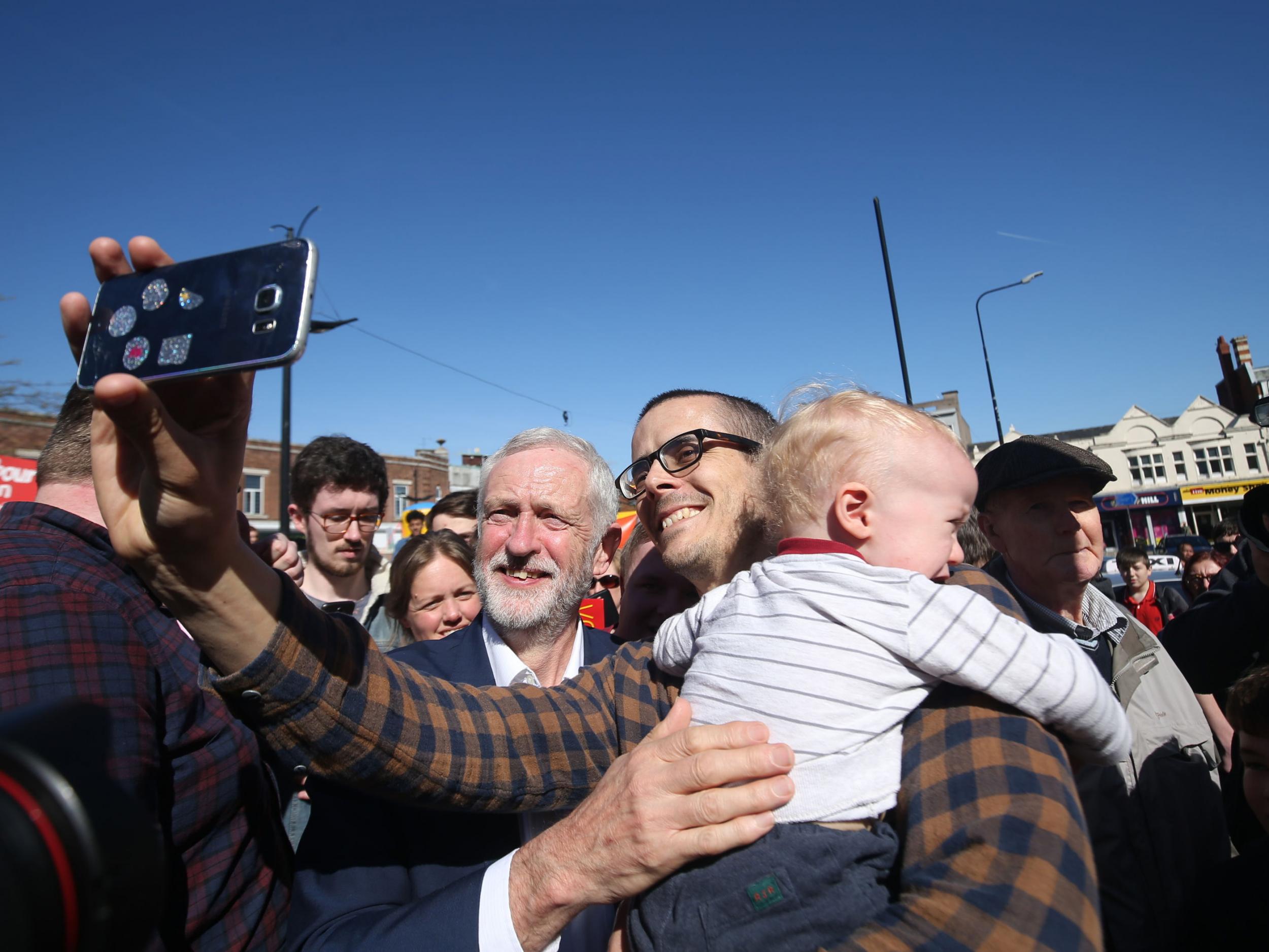 A man holds a child as he takes a selfie with Labour leader Jeremy Corbyn as he visits Crewe as part of Labour's general election campaign trail