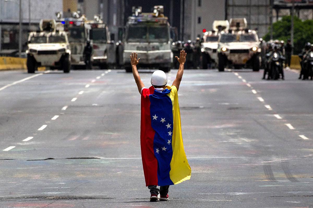 An opposition protestor, draped in a flag, stands in front of military police in Caracas