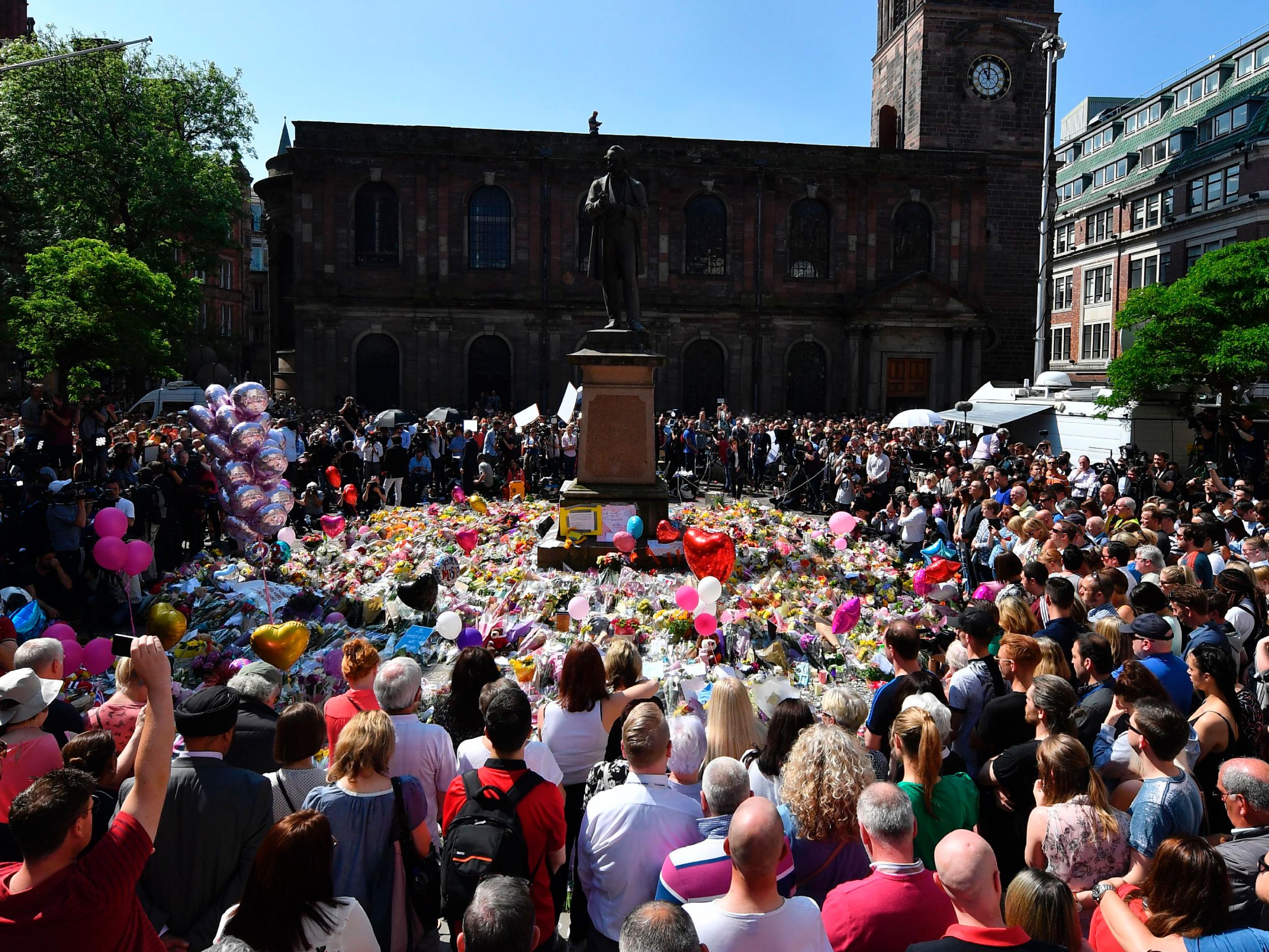 People stop to observe a minute's silence in St Ann's Square gathered around the tributes, in central Manchester