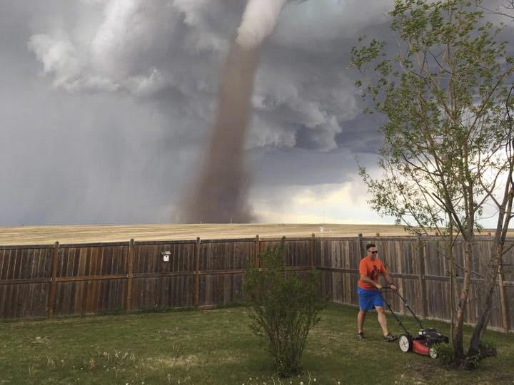 Theunis Wessels mows his lawn at his home in Three Hills, Alberta, as a tornado swirls ominously in the background