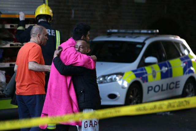 Two men hug within the security cordon as Grenfell Tower is engulfed by fire on June 14, 2017 in west London
