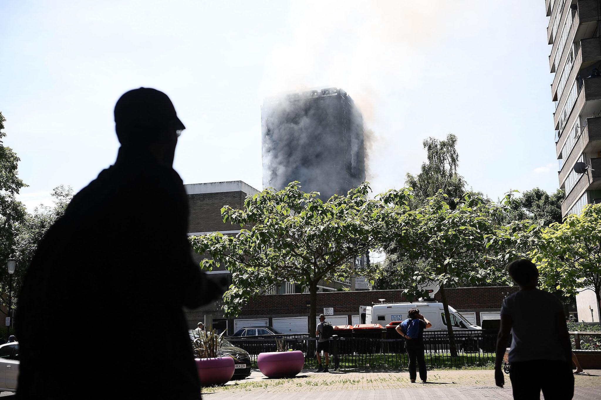 People watch from under the Westway near the burning 24 storey residential Grenfell Tower block in Latimer Road, West London on June 14, 2017 in London, England