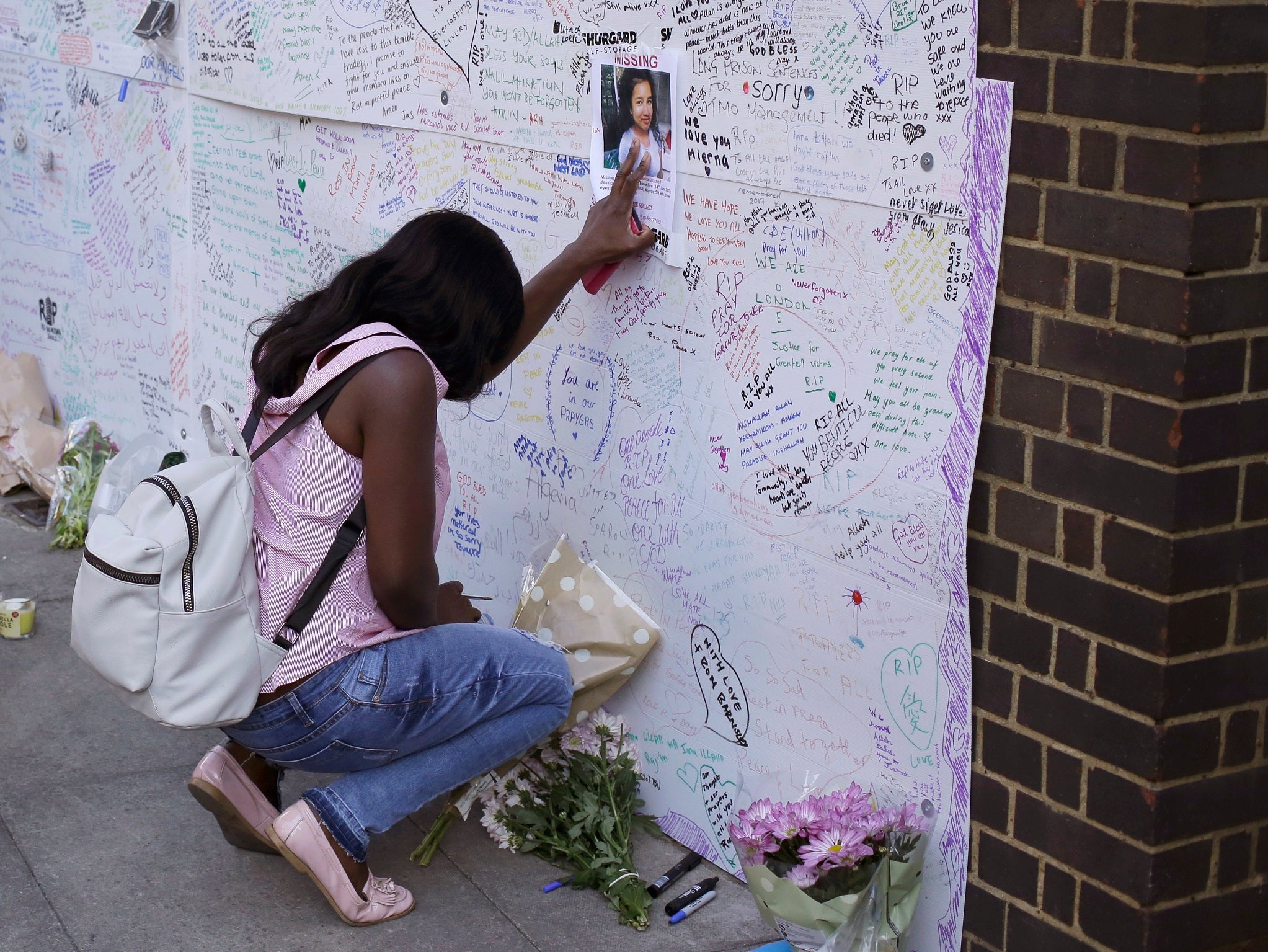 A woman touches a missing poster for 12-year-old Jessica Urbano next to the fire-gutted Grenfell Tower
