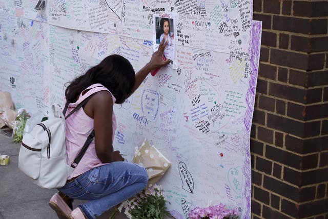 A woman touches a missing poster for 12-year-old Jessica Urbano next to the fire-gutted Grenfell Tower