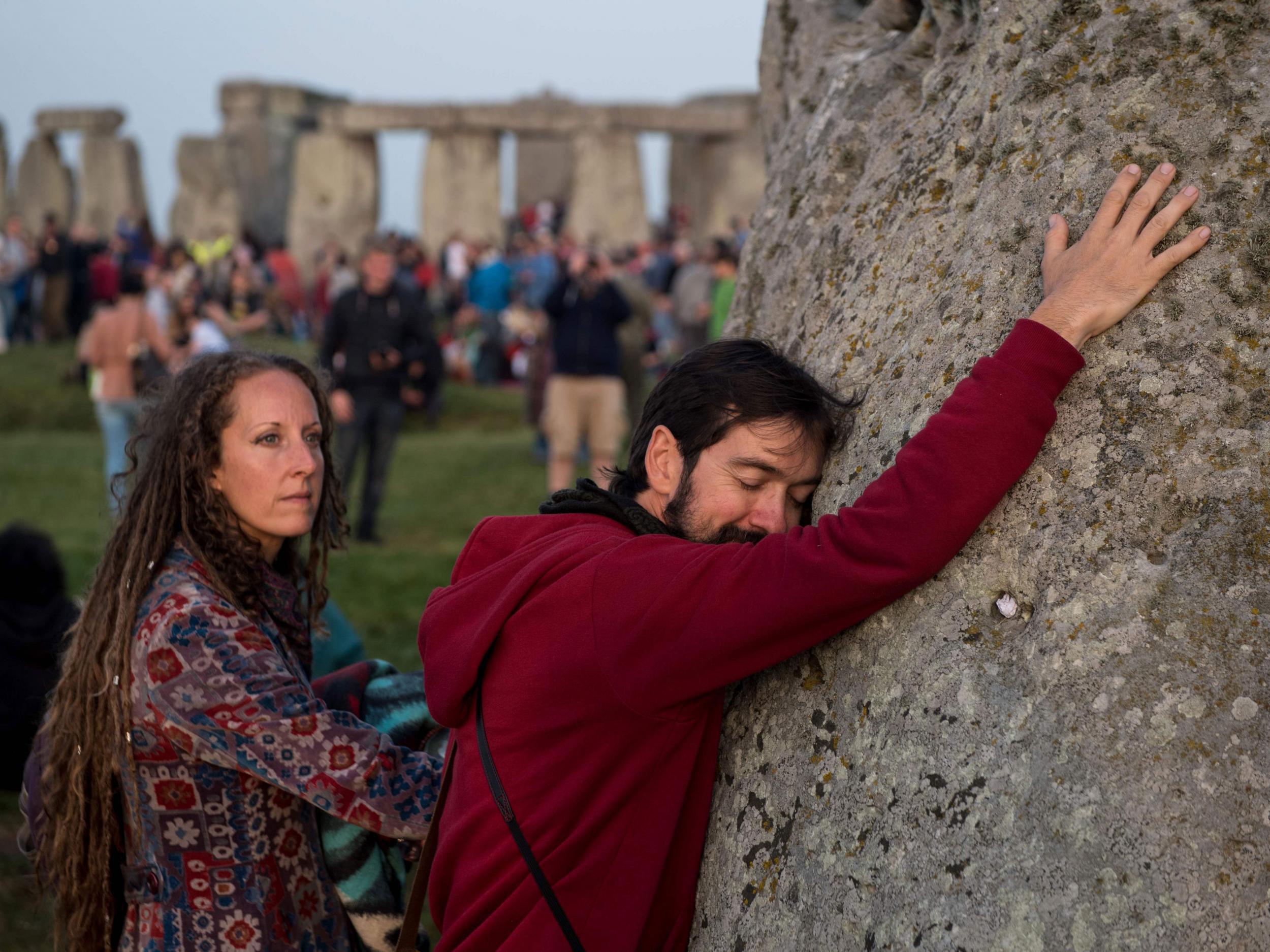 Revellers touch the Heel stone as people watch the sun rise