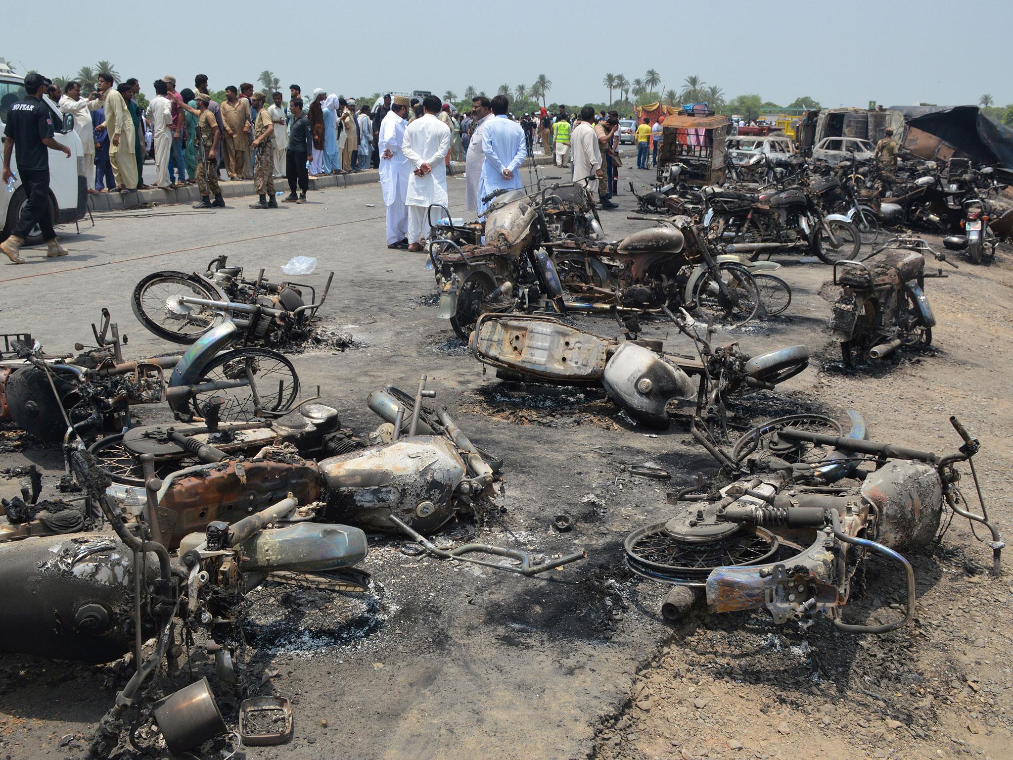 People gather behind burnt motorcycles and vehicles at the scene of an Oil tanker accident on the outskirts of Bahawalpur, Pakistan