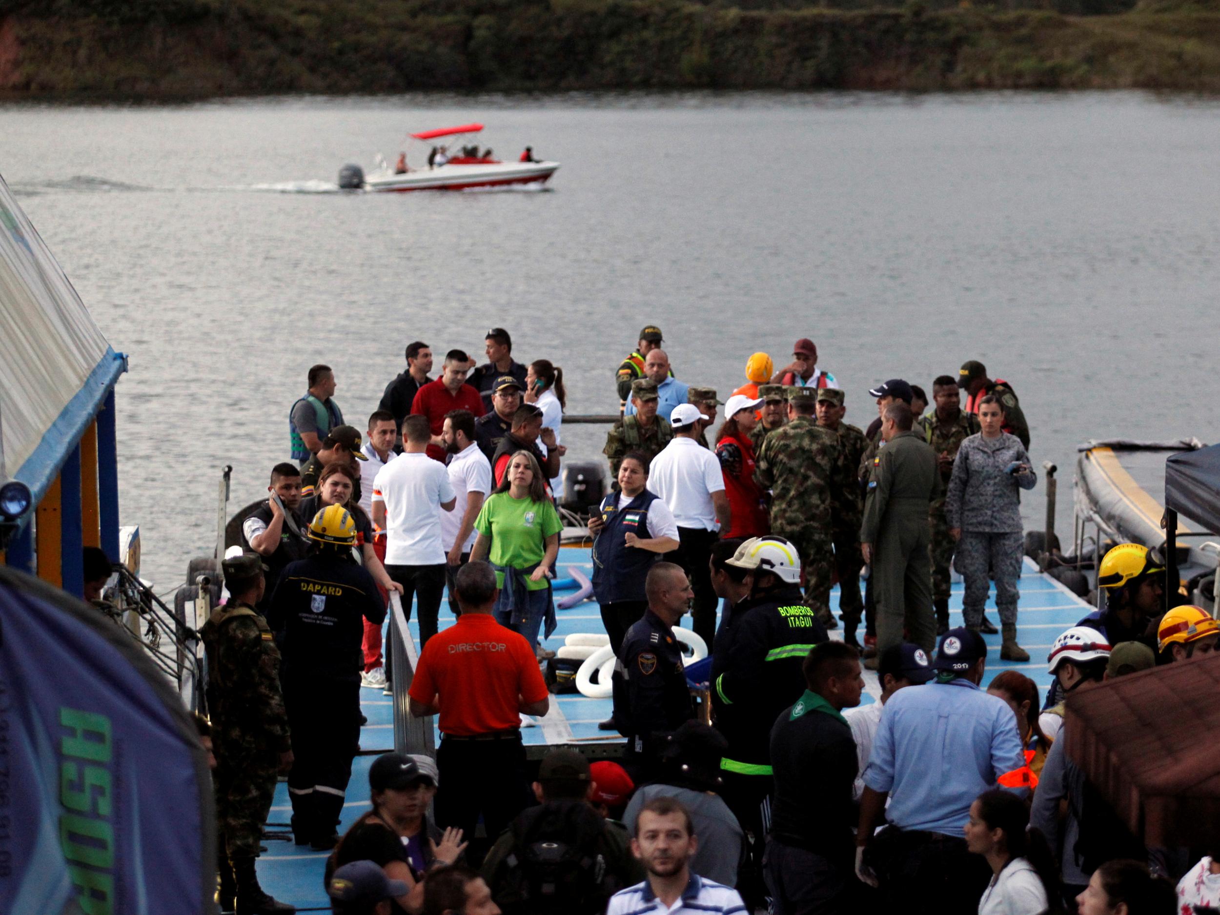 Anxious rescuer workers wait at the dock of the Guatape reservoir as a boat searches for further survivors