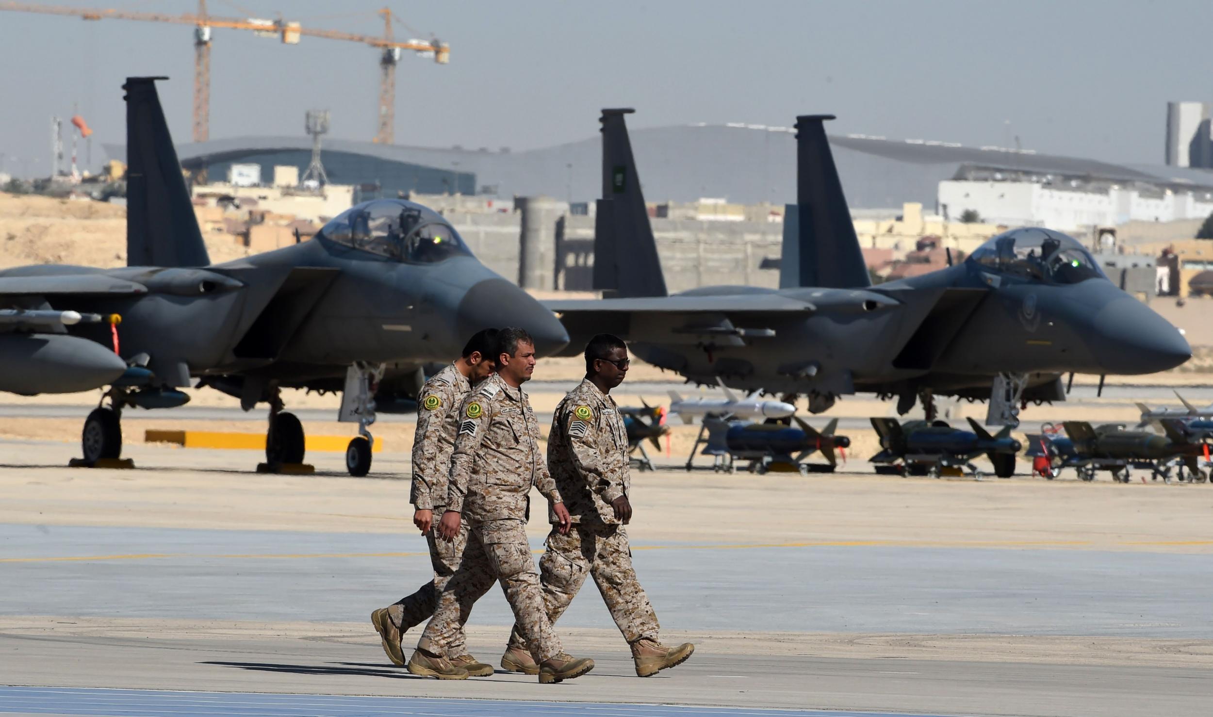 Saudi army officers walk past F-15 fighter jets, GBU bombs and missiles at King Salman airbase in Riyadh