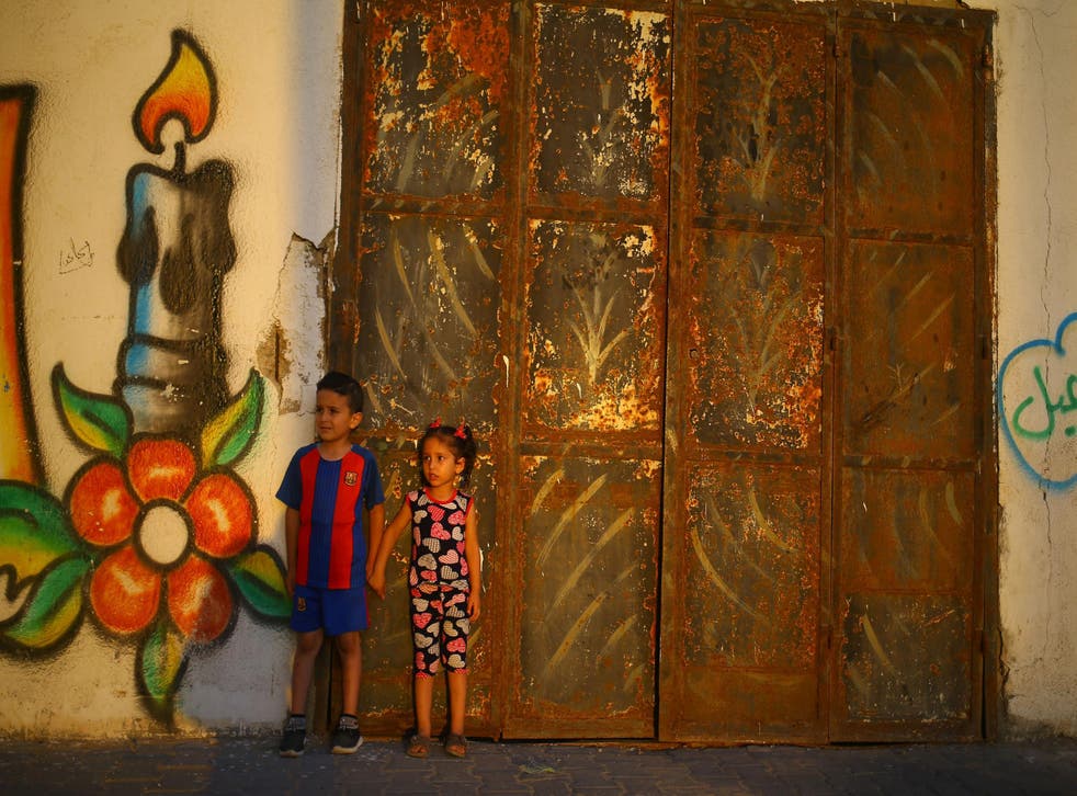 Palestinian children stand in front of a mural as the sun sets on 20 June 20 2017 in Gaza City