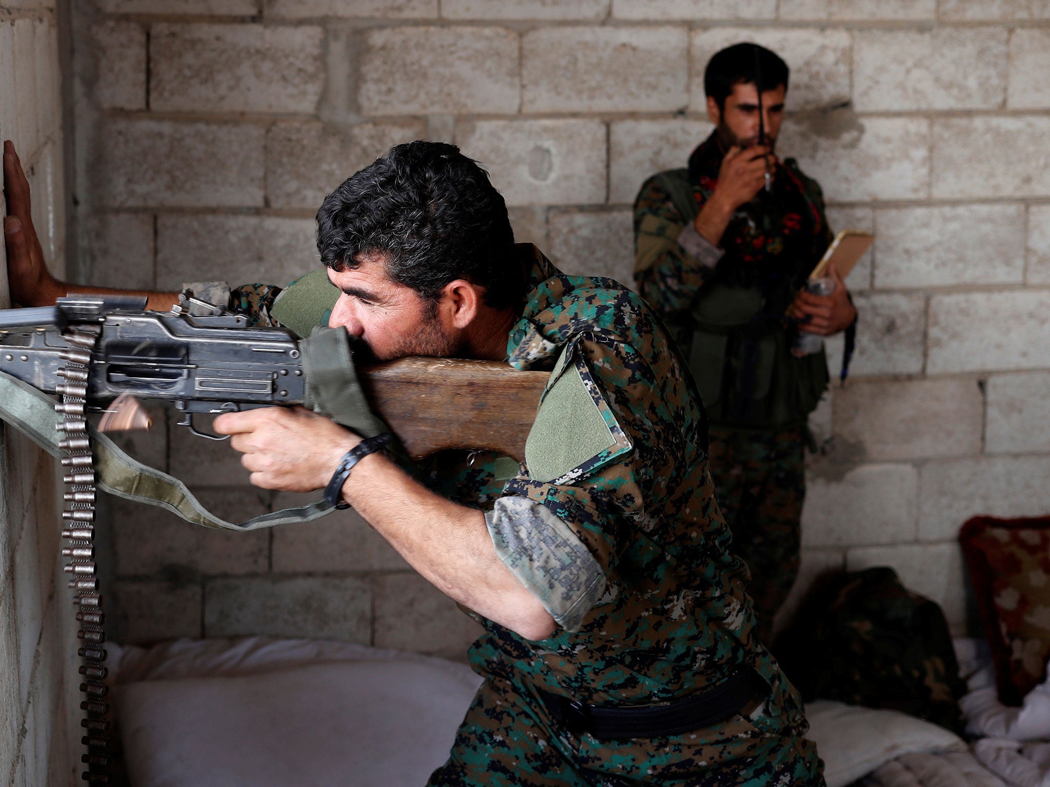 A Kurdish fighter from the People's Protection Units (YPG) fires his weapon from a house in Raqqa