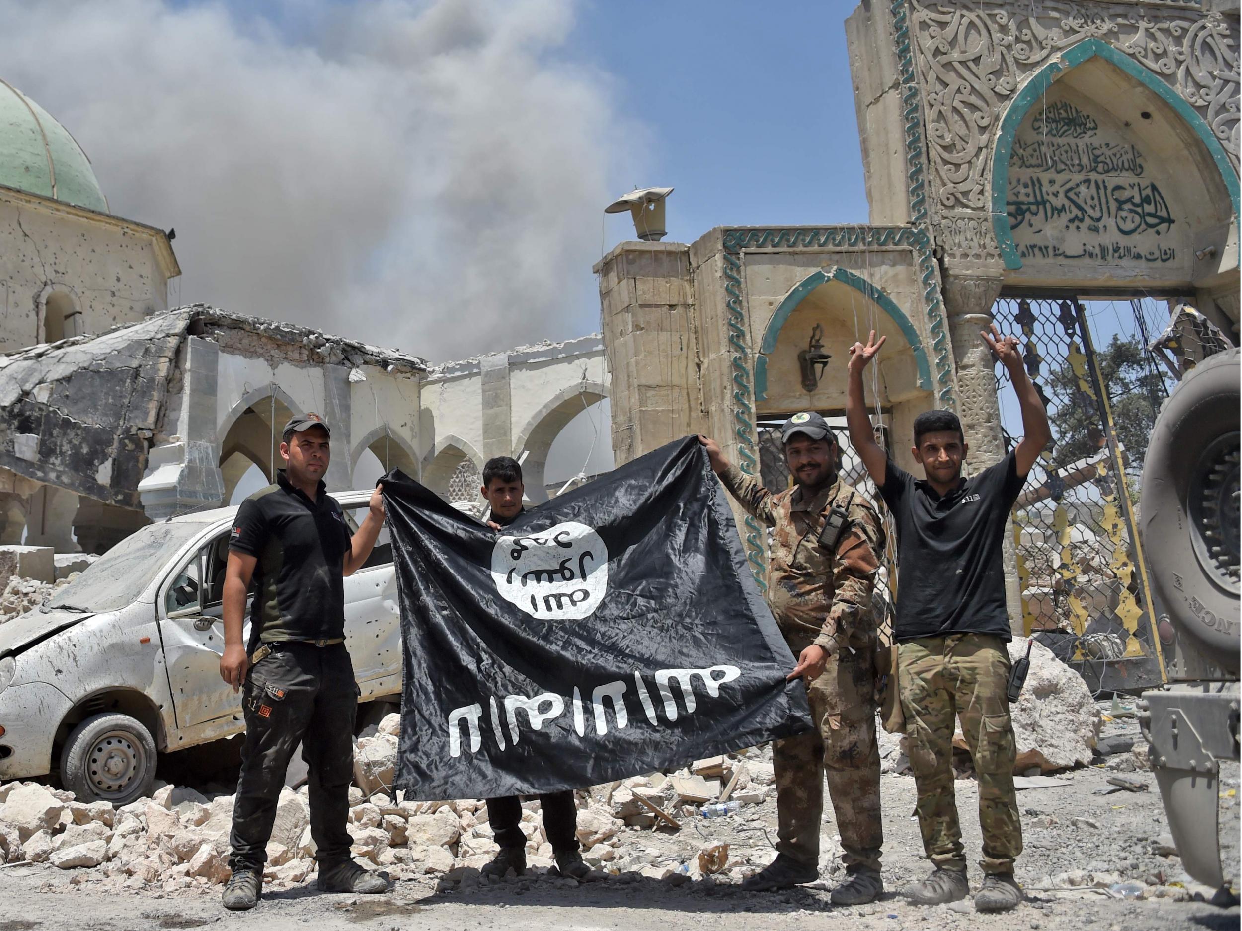 A member of the Iraqi Special Forces raises the victory gesture as others hold upside-down Isis flag outside the destroyed Al-Nuri Mosque in the Old City of Mosul, after the area was retaken