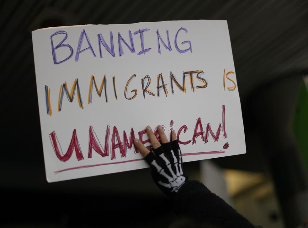 A protester holds up a sign that reads, 'Banning Immigrants is UnAmerican!,' as she stands with others at the Miami International Airport