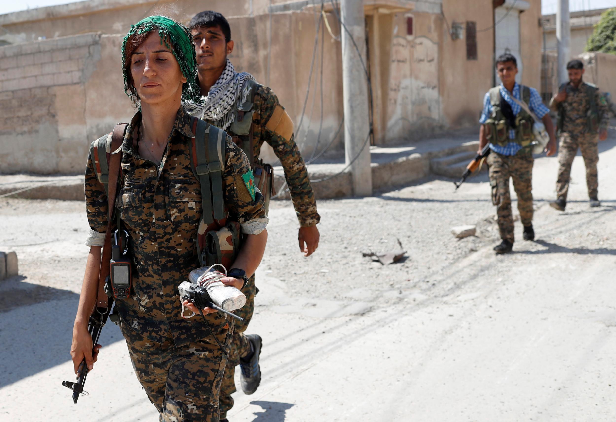 Kurdish People's Protection Units (YPG) fighters, part of the umbrella Syrian Democratic Forces (SDF), walk through a reclaimed neighbourhood of Raqqa on 16 June 2017