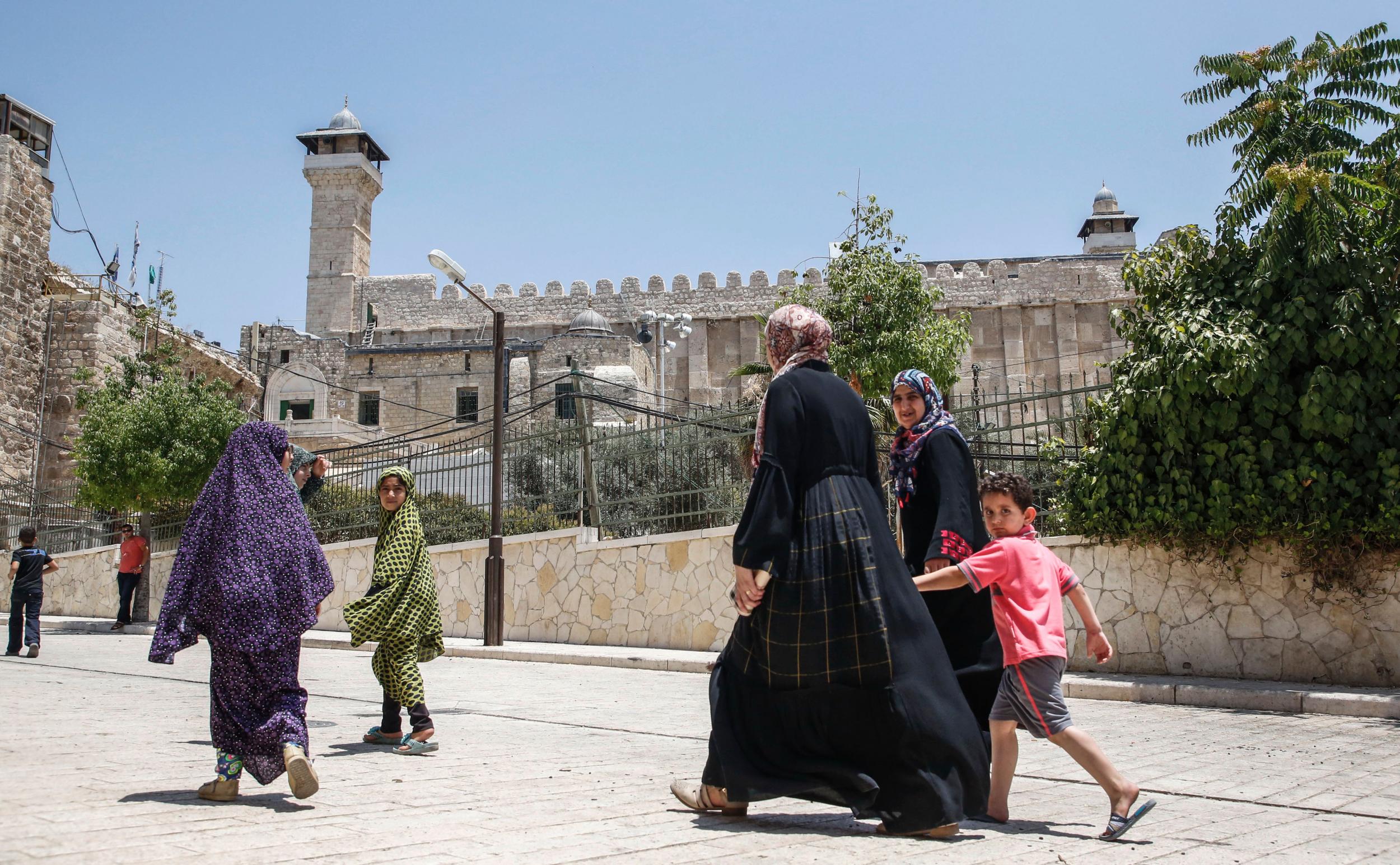 Families walk past the Cave of the Patriarchs, also known as the Ibrahimi Mosque, which is a holy shrine for Jews and Muslims, in the divided city of Hebron in the West Bank