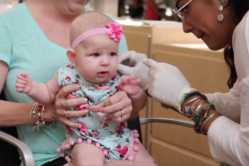 In the video, a young baby is being held by her mother as the salon worker attempts to place marker dots on her ears