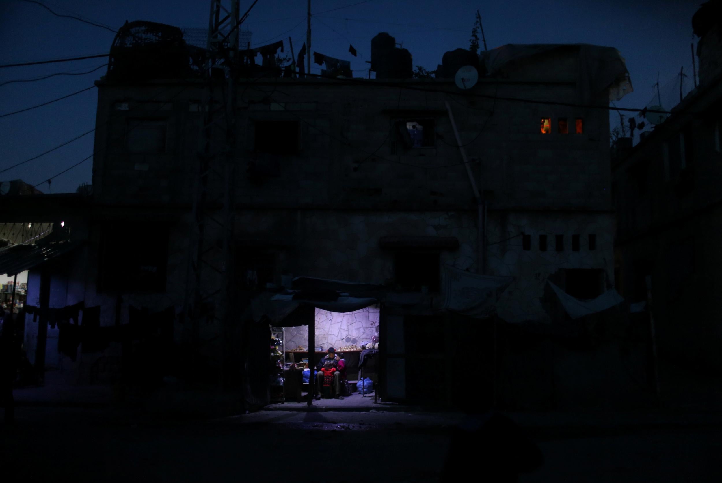 A man sells vegetables in a makeshift shop, lit with a lamp powered by a battery, during a power cut in Beit Lahiya in the northern Gaza Strip on 11 January 2017