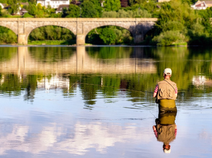 Man fly-fishing on the River Tweed with the iconic Kelso Bridge at the background in Kelso, Scotland