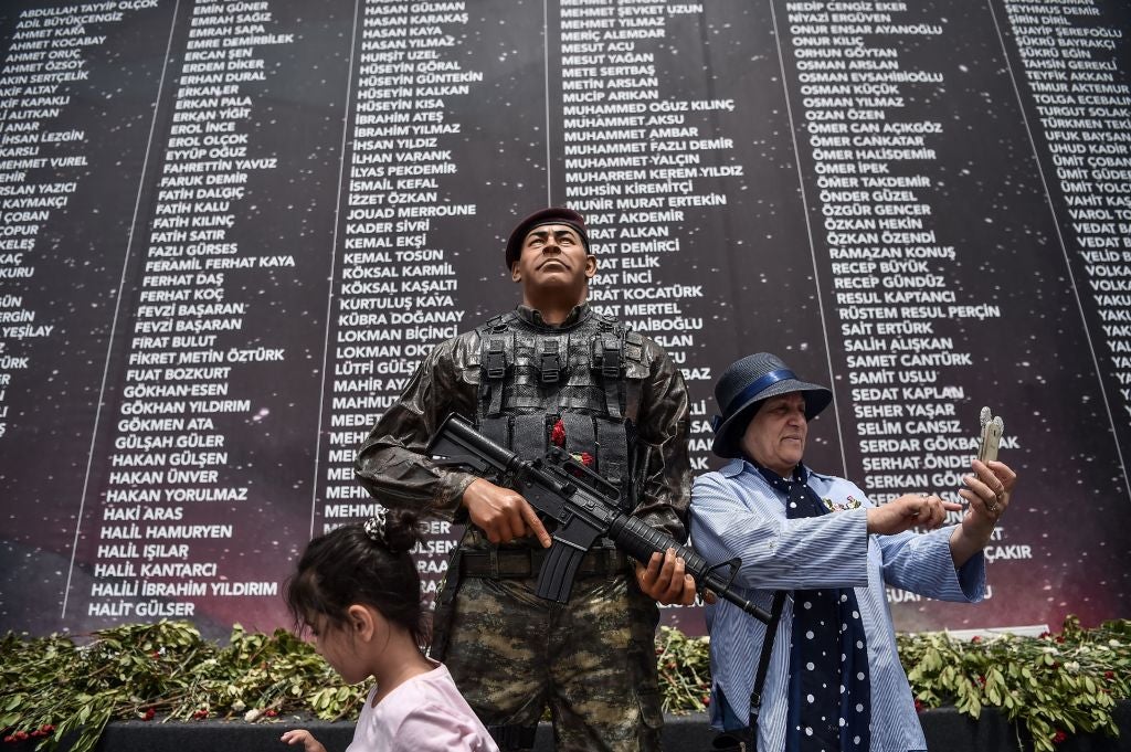 &#13;
A woman takes a selfie?next to the statue of Omer Halisdemir in Istanbul, in front of a memorial with the names of people killed last year during the failed coup attempt?&#13;