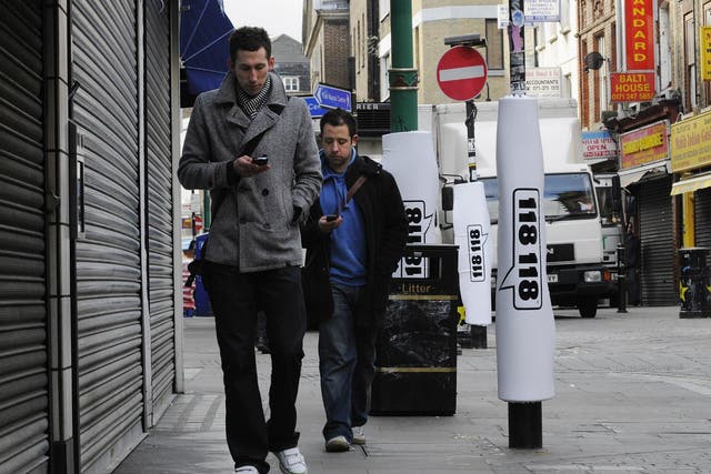 In this photo illustration, two pedestrians walks past padded lamp posts whilst texting in Brick Lane's 'Safe Text' street with padded lamposts. 