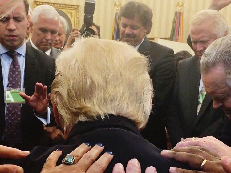 A group of people are shown laying their hands on US President Donald Trump, with Vice President Mike Pence, participating in the Oval Office prayer session at the White House in Washington