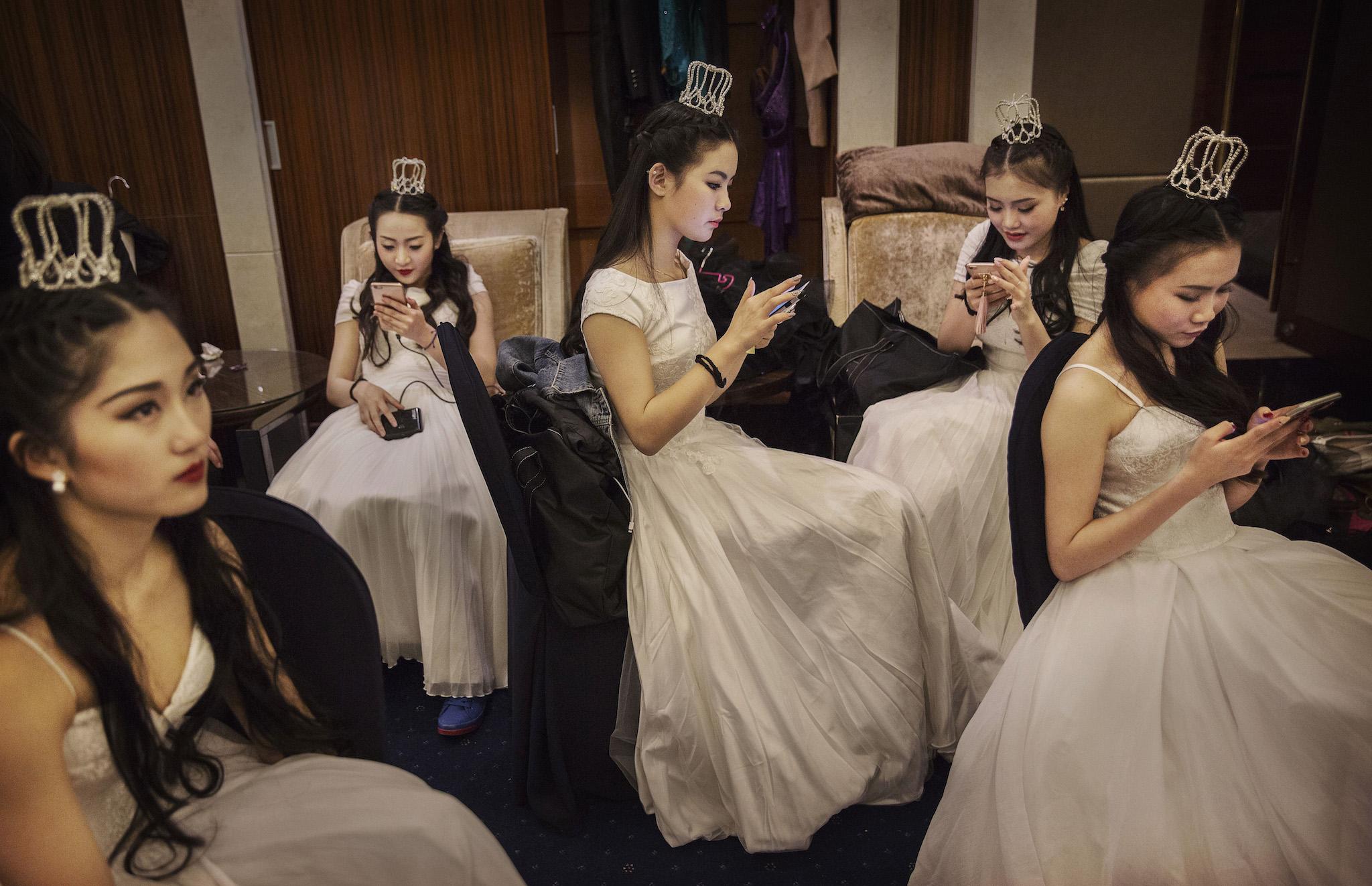 Debutantes from a local academy look at their mobile phones before taking part in the Vienna Ball at the Kempinski Hotel on March 19, 2016 in Beijing, China