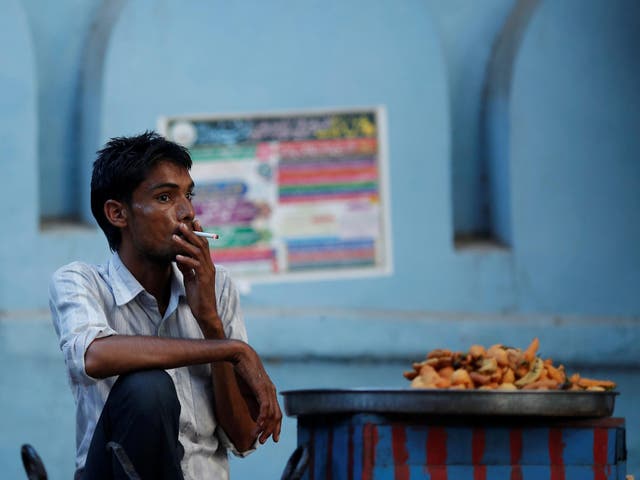 A snack vendor smokes a cigarette as he waits for customers on a street in New Delhi