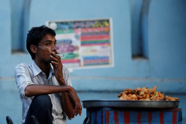 A snack vendor smokes a cigarette as he waits for customers on a street in New Delhi