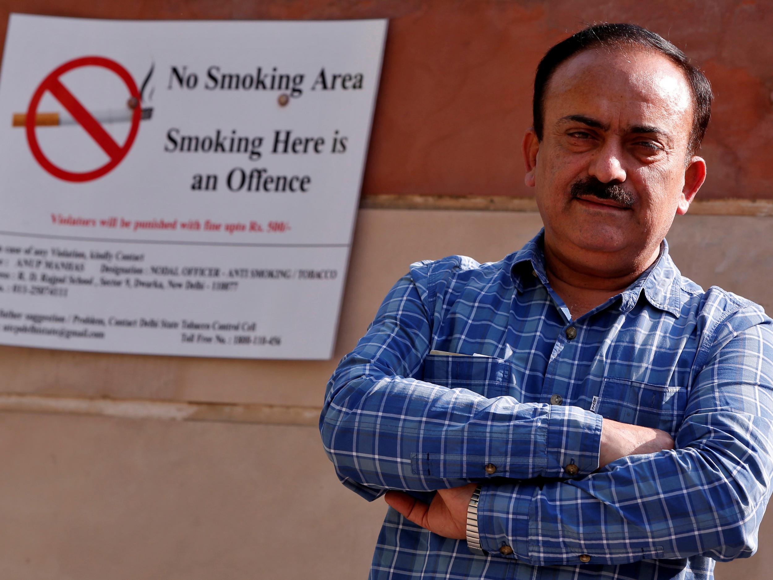 S.K. Arora, chief tobacco control officer of Delhi's stae goverment, poses for a photogrph next to an anti-tobacco sign pasted on a school wall alongside a road in New Delhi