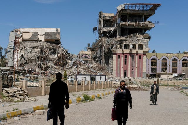 People walk in front of the remains of a building at the University of Mosul, which was burned and destroyed in the nine-month-long fight to oust Isis from the city