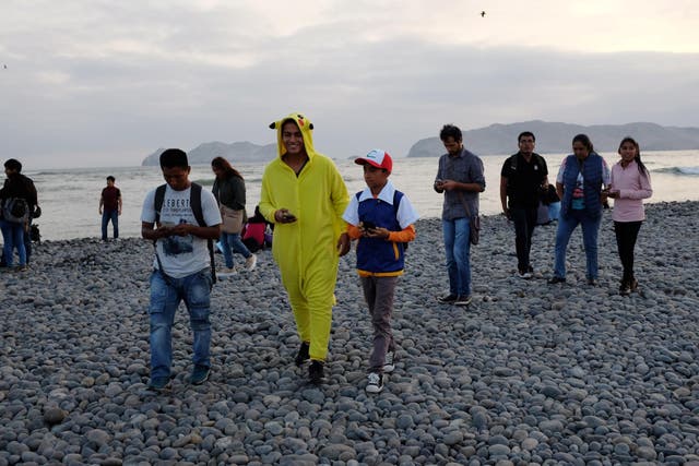 People walk with their mobile phones as some play Pokemon GO at La Punta beach in Callao, Peru