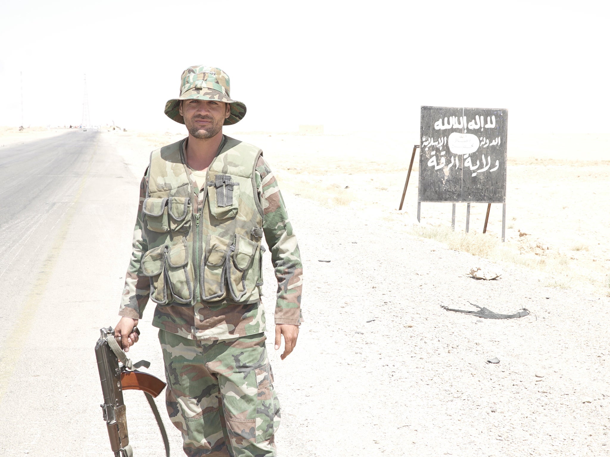 A Syrian soldier in front of a sign on the main road from Homs, ‘welcoming’ visitors to the Isis ‘Caliphate-Province of Raqqa’