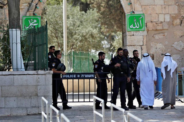 Palestinians walk next to Israeli security forces at the entrance of the compound