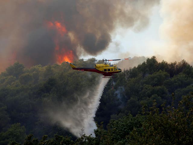 A helicopter drops water as flames and smoke from a burning wildfire fills the sky in Carros, near Nice