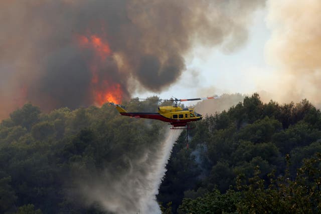 A helicopter drops water as flames and smoke from a burning wildfire fills the sky in Carros, near Nice