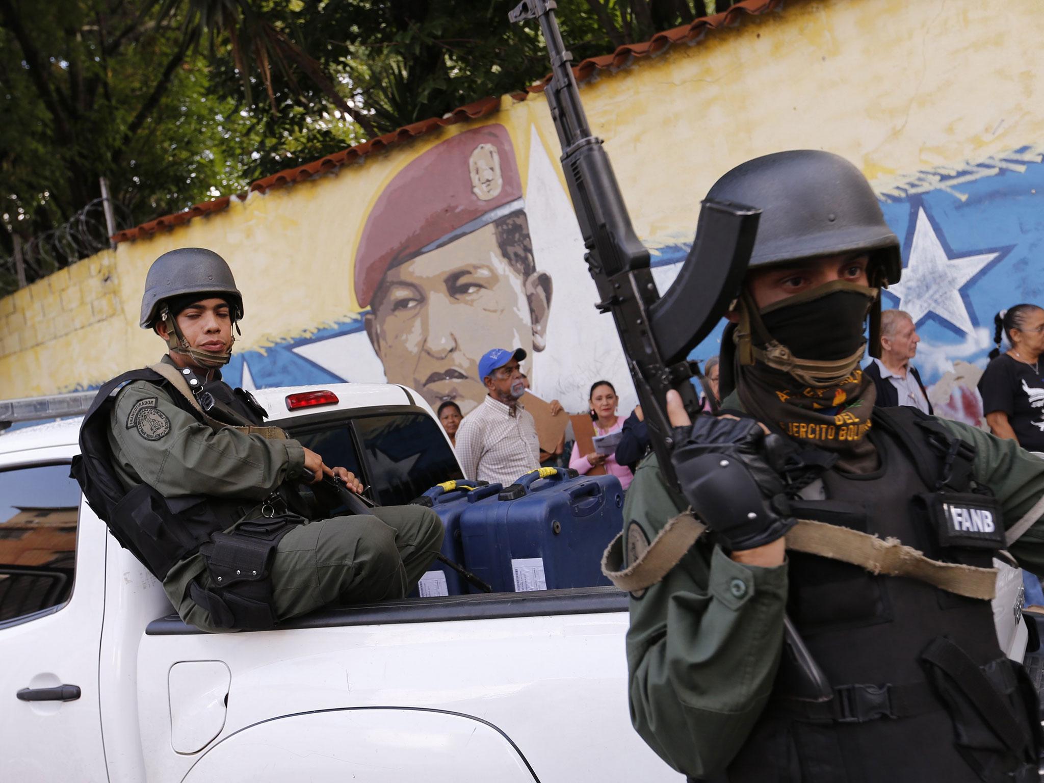 Soldiers stand guard as people wait in line in front of a mural of the late Venezuelan President Hugo Chavez before casting their votes at a polling station during the Constituent Assembly election in Caracas, Venezuela