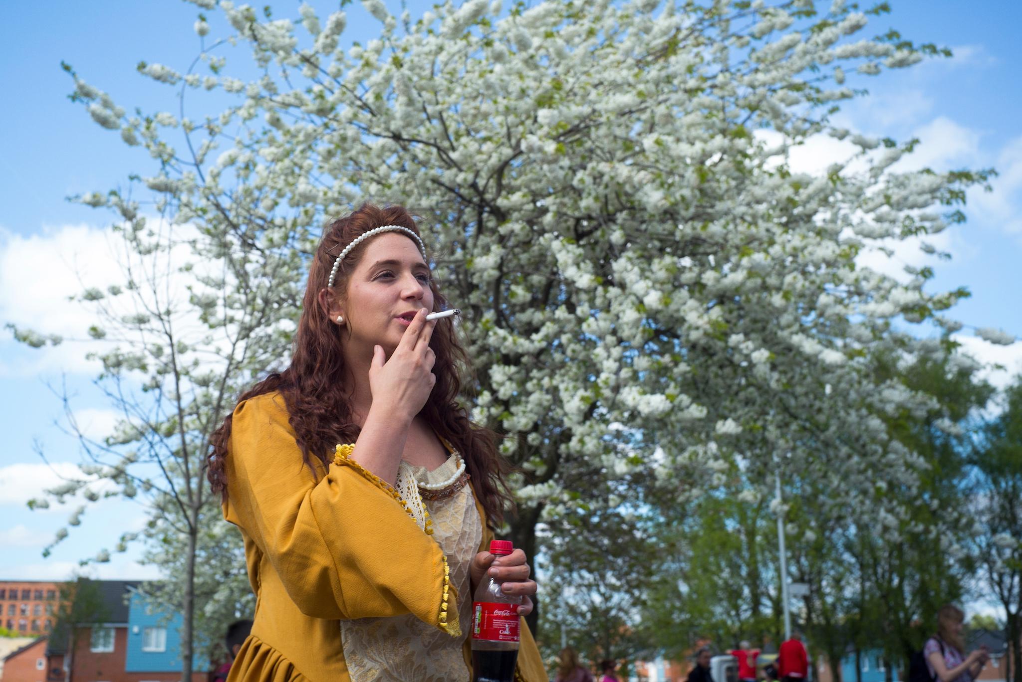 A woman smokes as families and local residents watch the Manchester St George's Day parade
