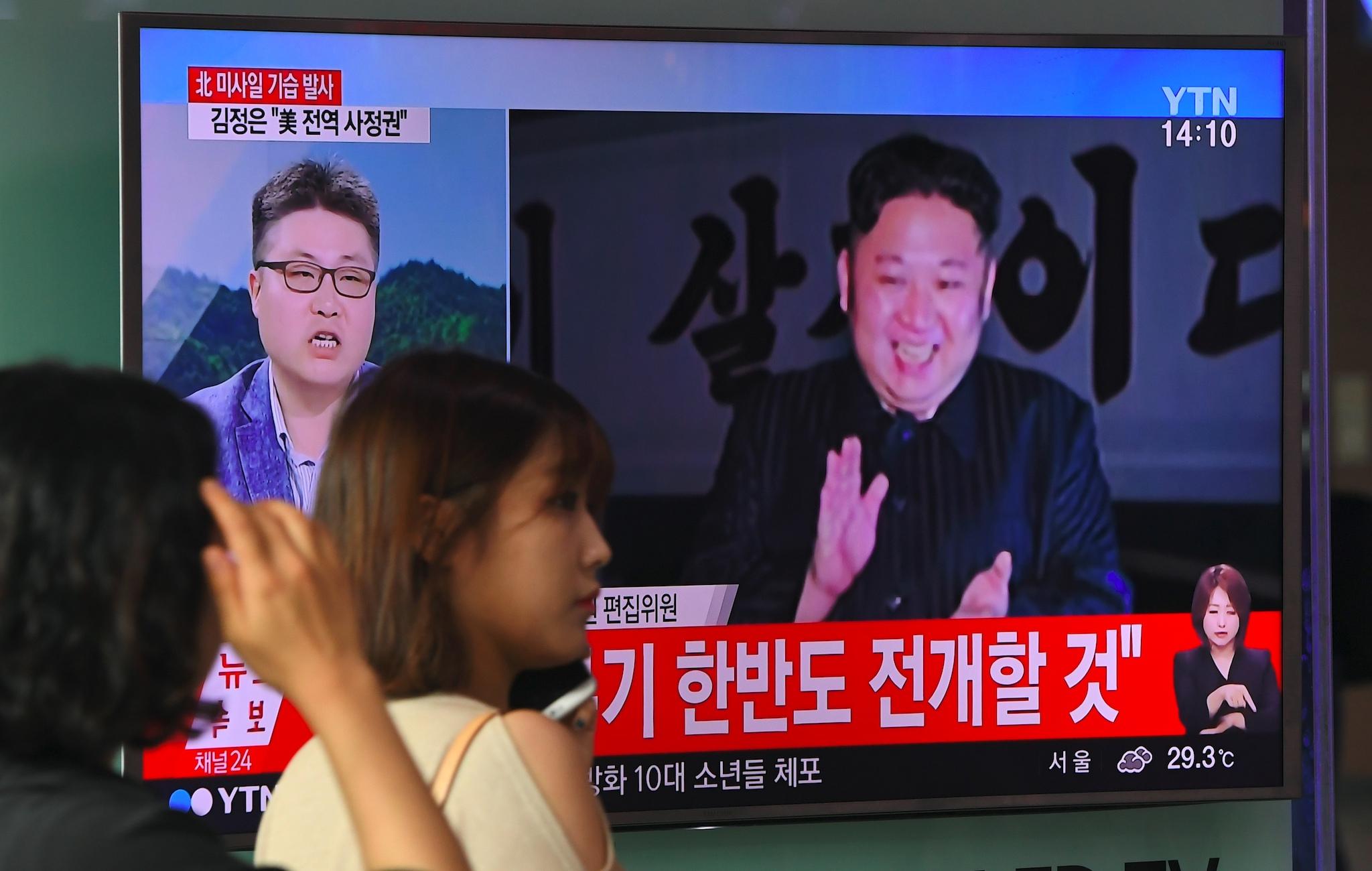 A woman at a railway station in Seoul walks past a television screen showing a video footage of North Korean leader Kim Jong-Un celebrating his country's latest test launch of an intercontinental ballistic missile