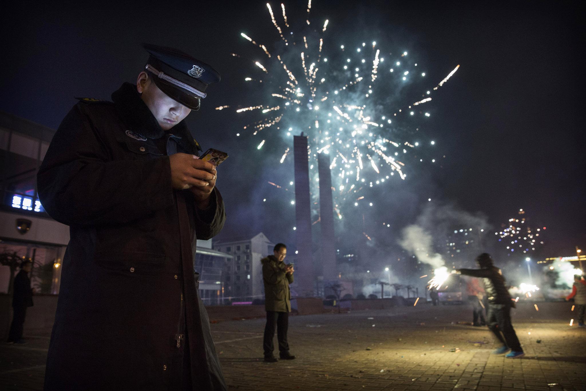 A Chinese security guard checks his smartphone as fireworks explode during celebrations of the Lunar New early on February 19, 2015 in Beijing, China