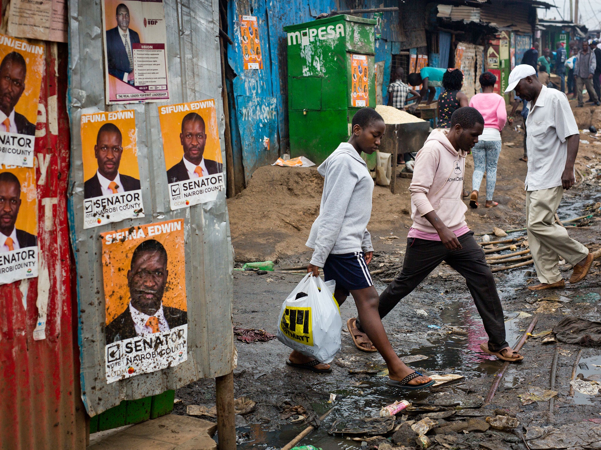 Kenyans walk past election posters in Nairobi's Kibera slum; rising living costs and inadequate healthcare are among the issues facing the country