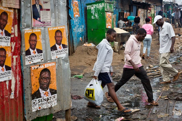 Kenyans walk past election posters in Nairobi's Kibera slum; rising living costs and inadequate healthcare are among the issues facing the country
