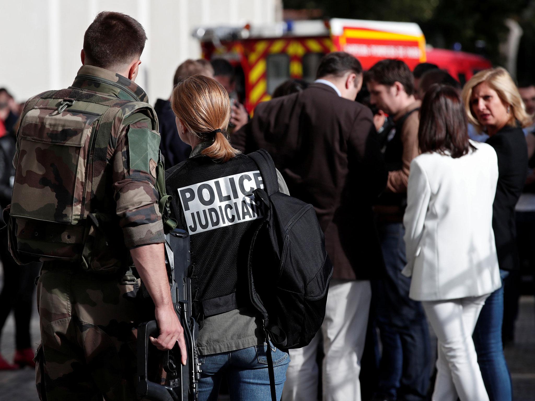 A police investigator and an armed soldier work near the scene