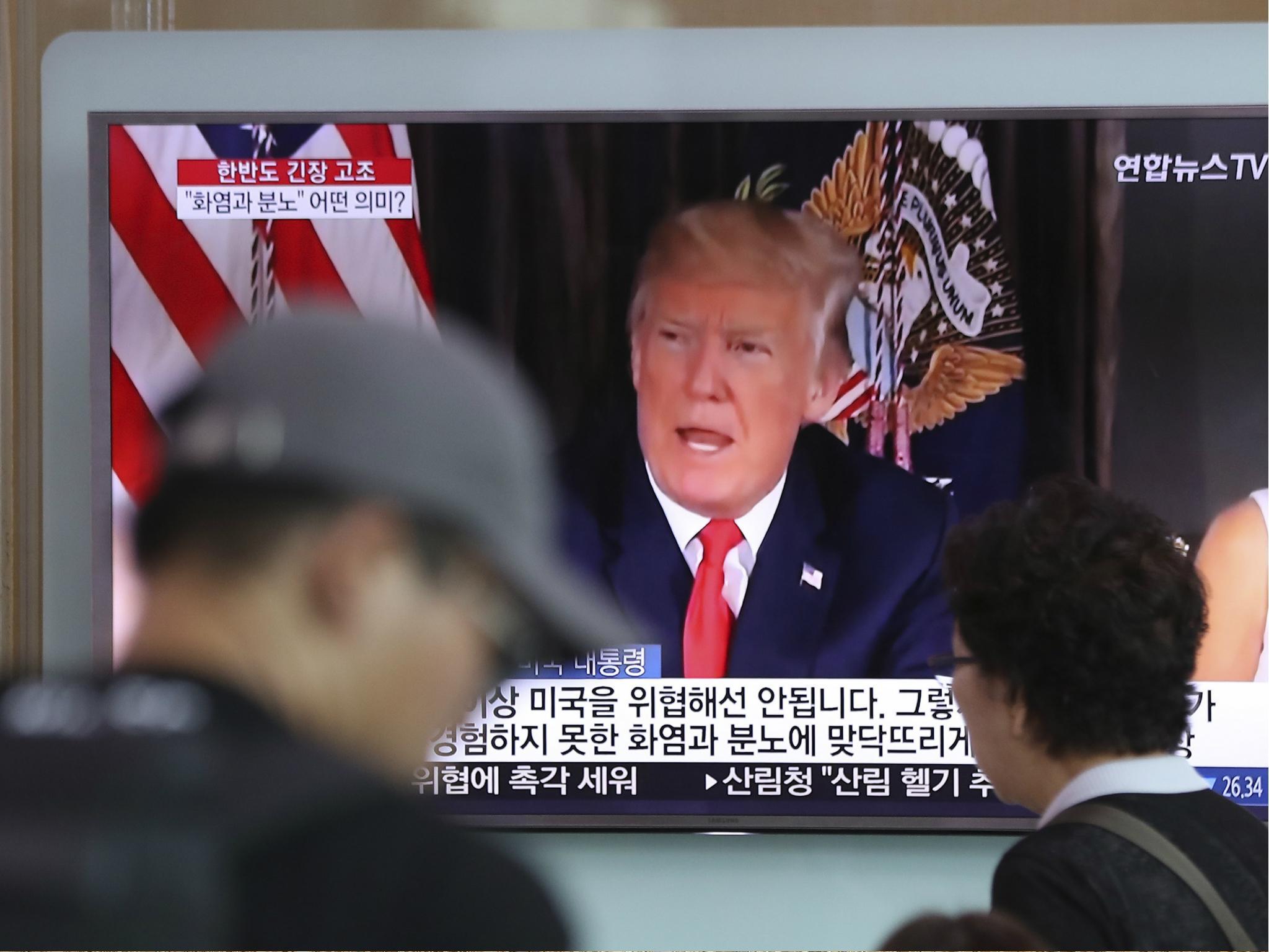 People walk by a TV screen showing a local news program reporting with an image of U.S. President Donald Trump at the Seoul Train Station in Seoul, South Korea on 9 Aug 2017.