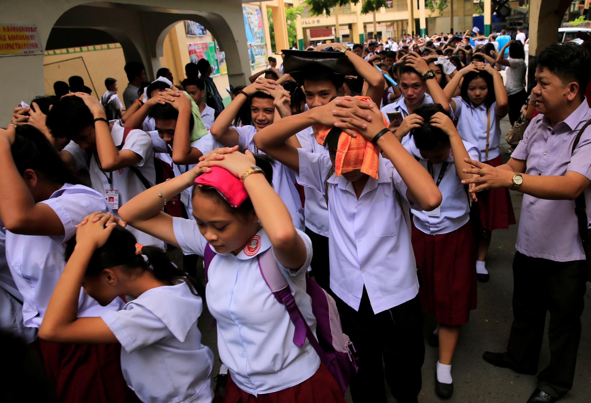 Students use their hands to cover their heads as they evacuate their school premises after an earthquake of magnitude 6.2 hit the northern island of Luzon
