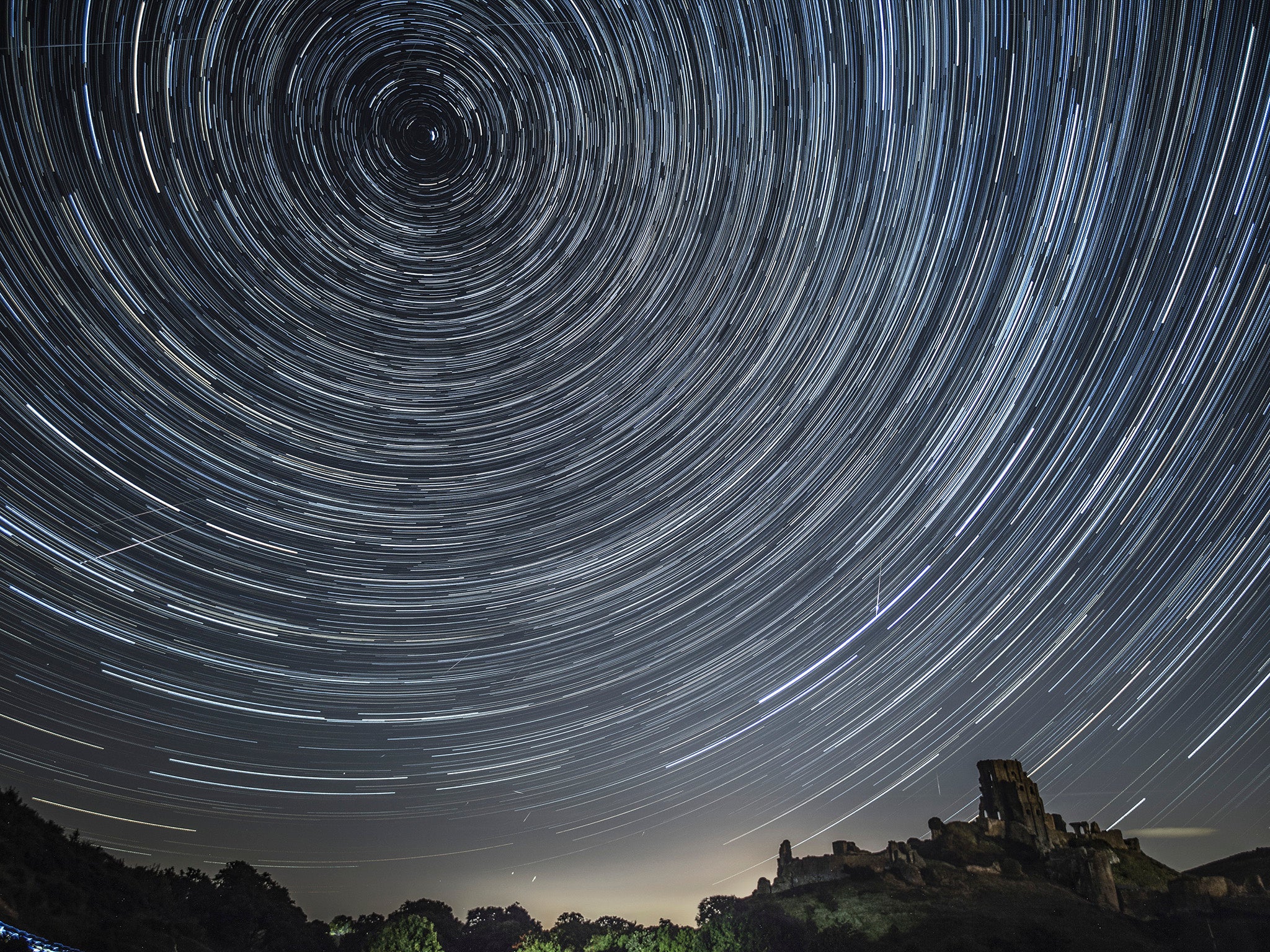 Comets streak across the night sky beneath stars that appear to rotate in a long-exposure photograph taken above Corfe Castle on August 12, 2016 in Corfe Castle in Dorset.