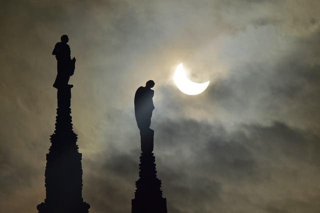 A partial solar eclipse of the sun is visible next to the statues of Milan's cathedral on March 20, 2015