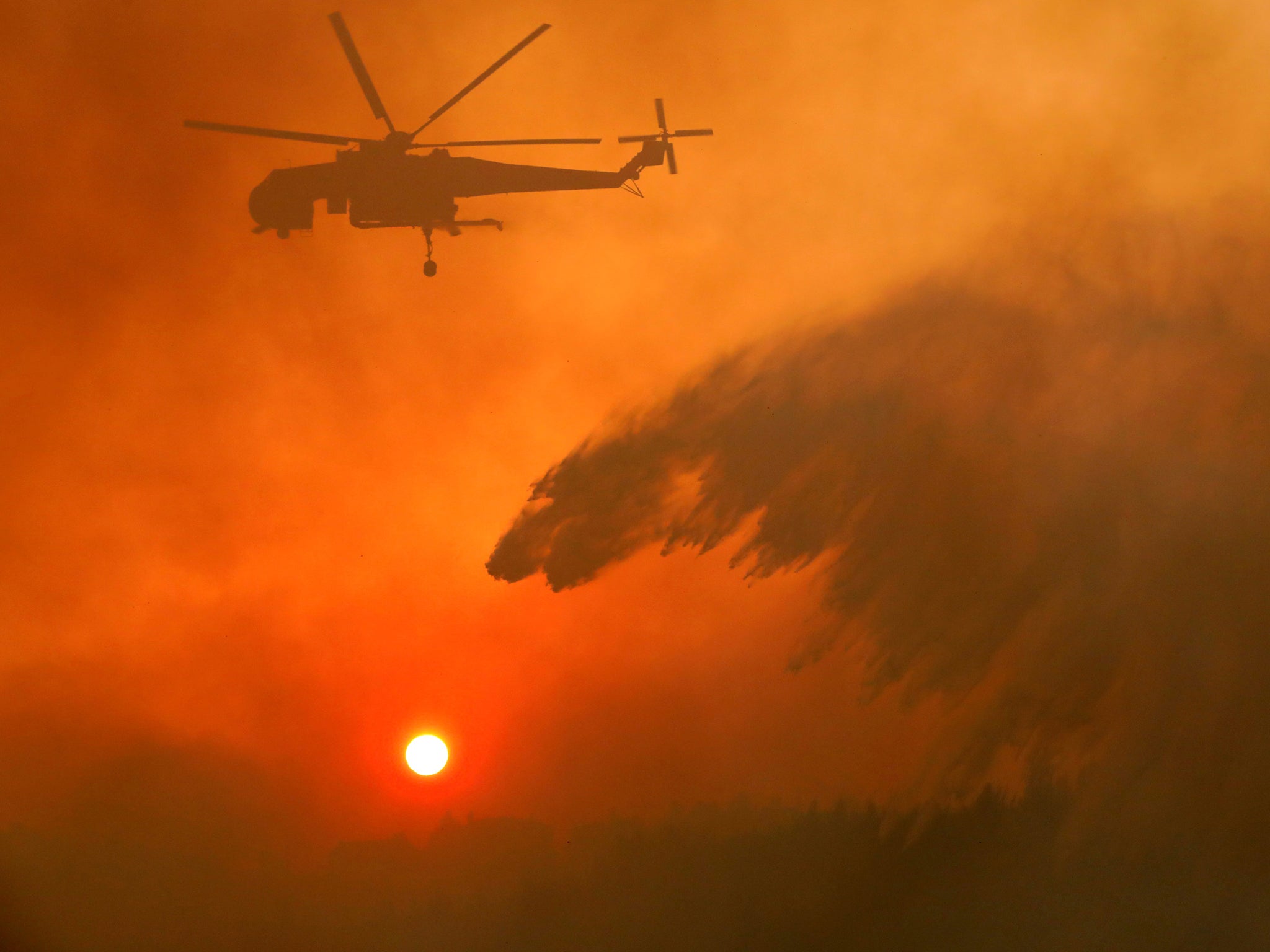 A firefighting helicopter makes water drop as a wildfire burns near the village of Metochi, north of Athens, Greece